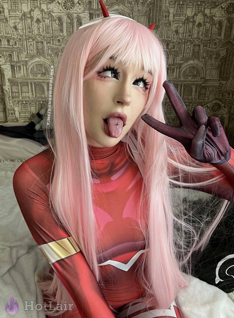 Hot Zero Two cosplay girl with long pink hair in red bodysuit sticking tongue out and making peace sign