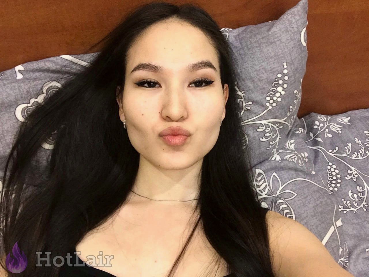 Cute Asian beauty lying on bed making kissy face with long black hair