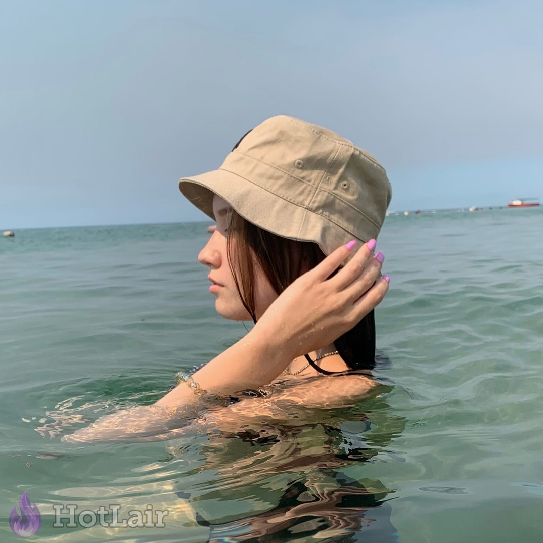 Beautiful girl in beige bucket hat standing in ocean water, beach portrait