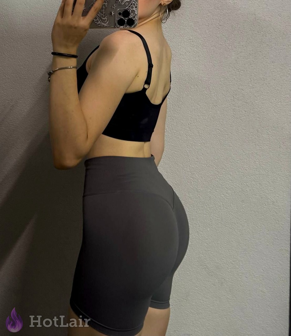 Athletic girl in black crop top and tight grey shorts showing her round bubble butt in mirror