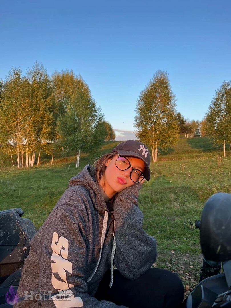 Cute young woman with glasses and hoodie relaxing outdoors in nature at sunset