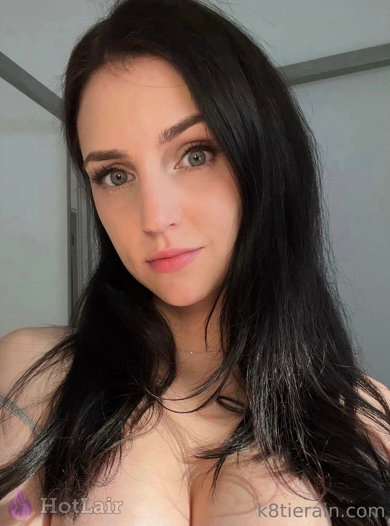 Beautiful brunette with long black hair and striking green eyes posing topless with perfect cleavage and subtle smile in soft light