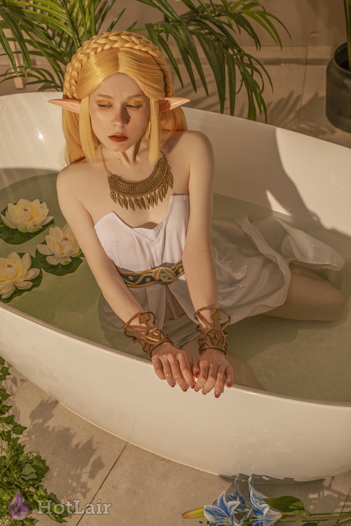 Blonde elf in white outfit sitting gracefully in a white bathtub surrounded by lotus flowers and green plants
