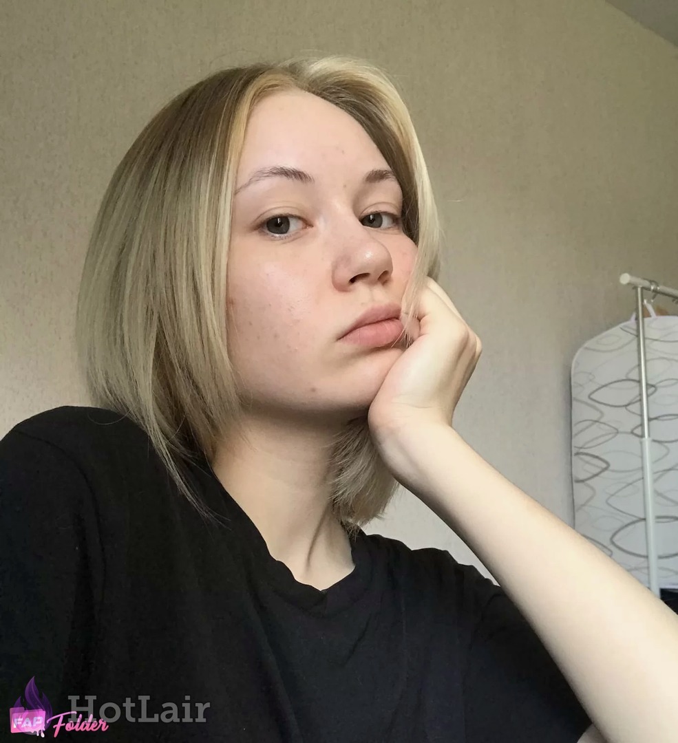 Blonde woman with shoulder-length hair in black t-shirt posing with hand on cheek, soft natural light portrait