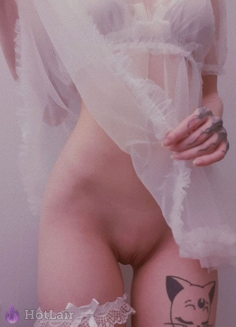 Beautiful woman in sheer white babydoll lingerie and lace stockings, tattooed hand on hip with cute cat tattoo on thigh