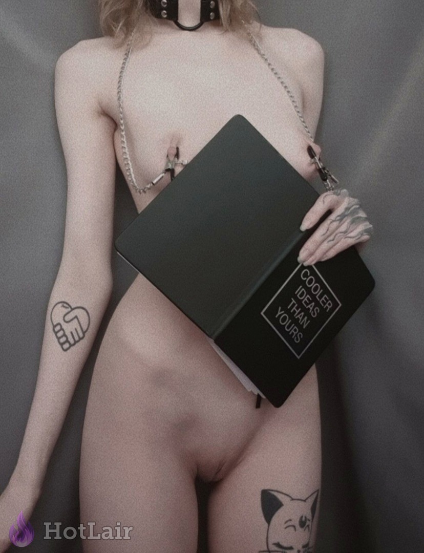 Nude tattooed blonde wearing black choker and nipple clamps with chains, holding black book “Cooler Ideas Than Yours” seductively