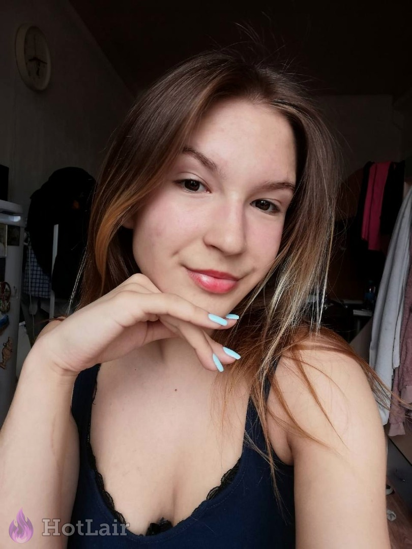 Pretty brunette with light brown hair smiling at camera in low-cut black top, hand gently on chin, natural beauty selfie