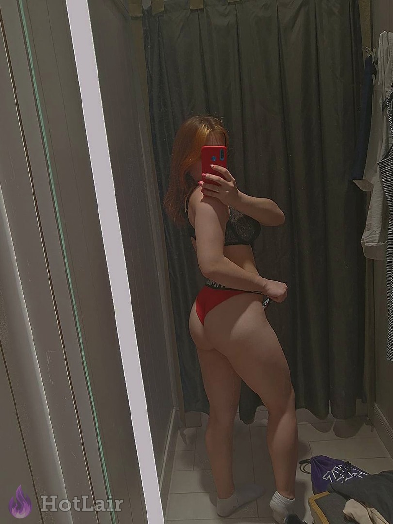 Attractive red-haired woman posing in bathroom mirror wearing black bra and bright red panties, full body view