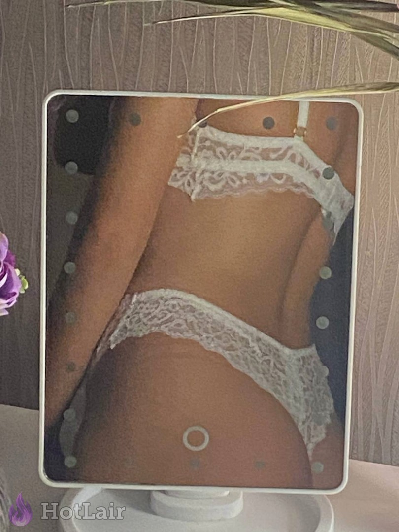 Seductive back view of slim girl in white lace lingerie set reflected in illuminated vanity mirror