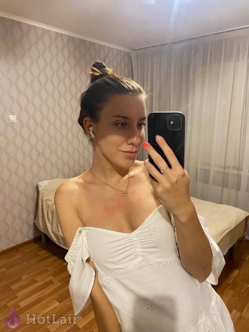 Pretty brunette in white off-shoulder dress taking mirror selfie, showing nice cleavage in bedroom