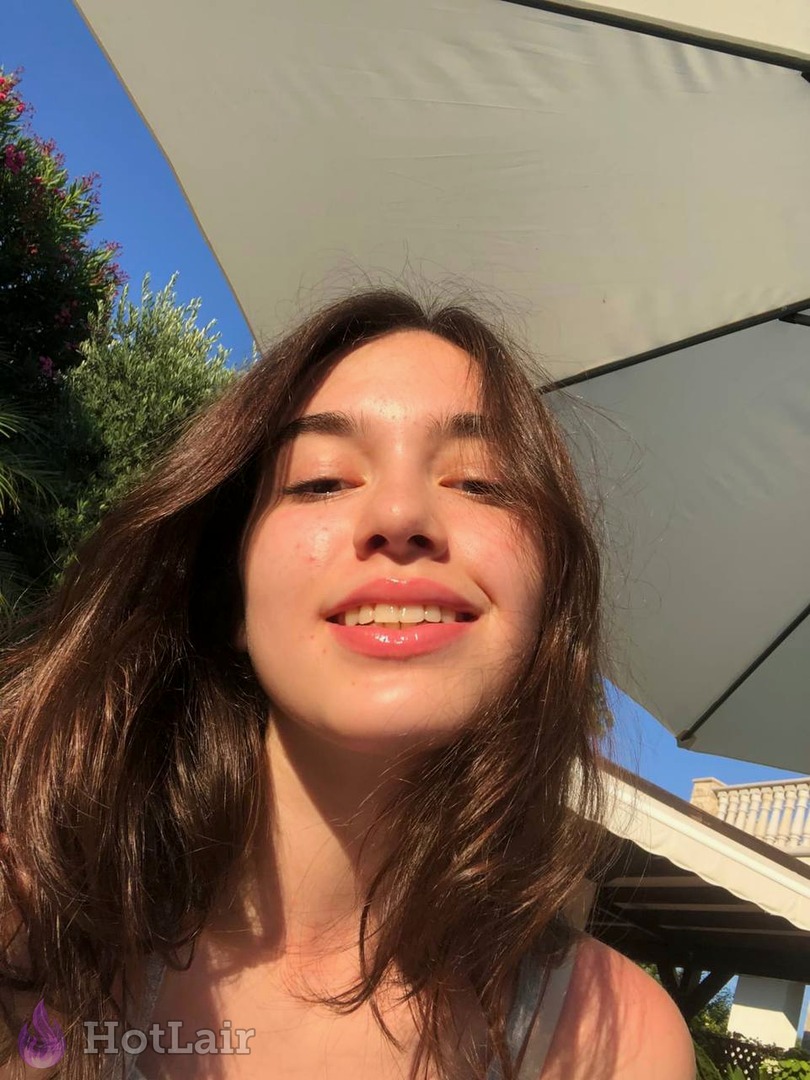 Beautiful young brunette smiling at camera in bright outdoor selfie under umbrella on sunny day