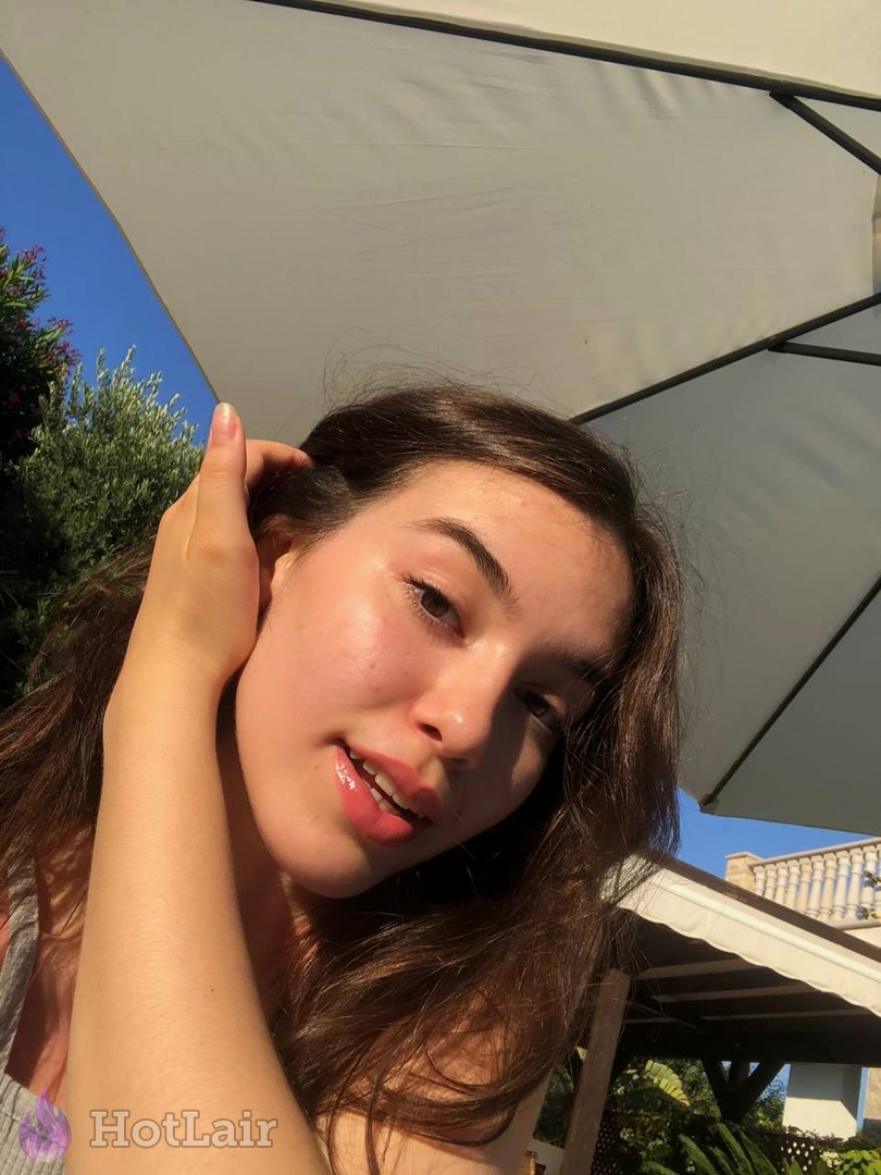 Close-up portrait of pretty brunette with glossy lips posing outdoors, hand touching her hair seductively