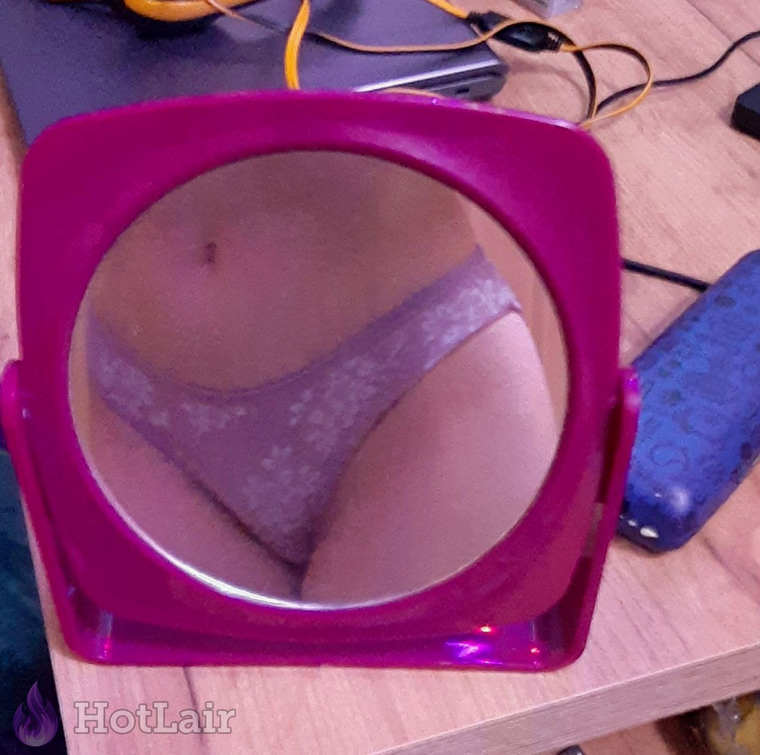 Mirror reflection of girl’s lower body in floral panties captured in pink vanity mirror on wooden desk