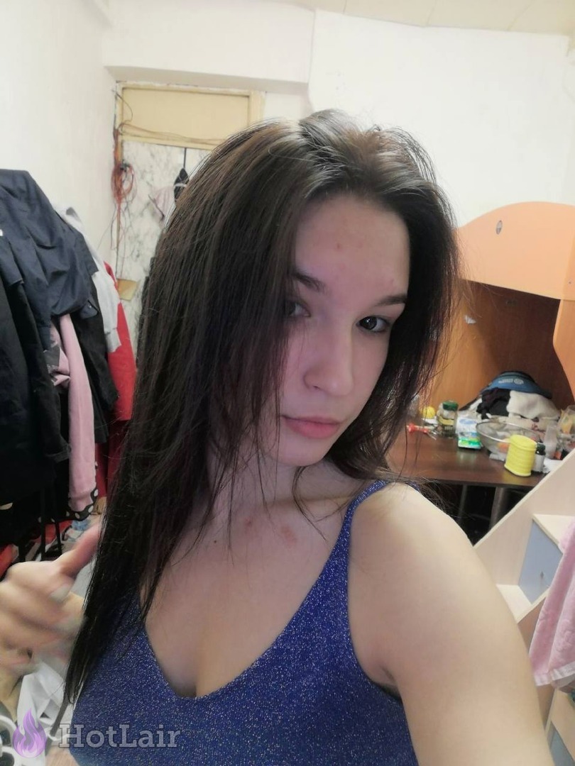 Natural brunette taking casual selfie in sparkly blue tank top, showing cleavage and long hair with thumbs up