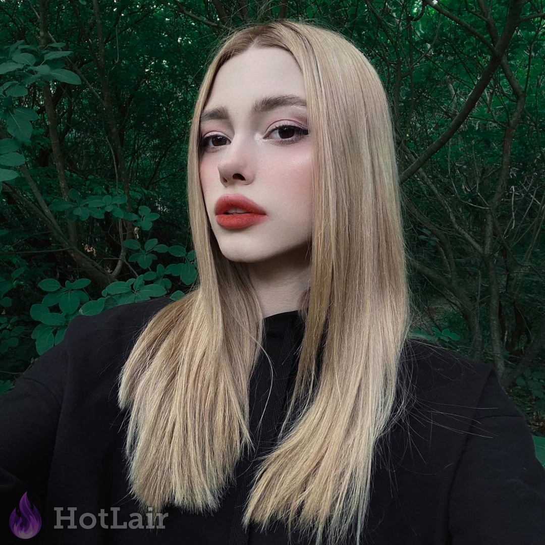 Pretty blonde with long hair and red lips posing seductively in a green forest