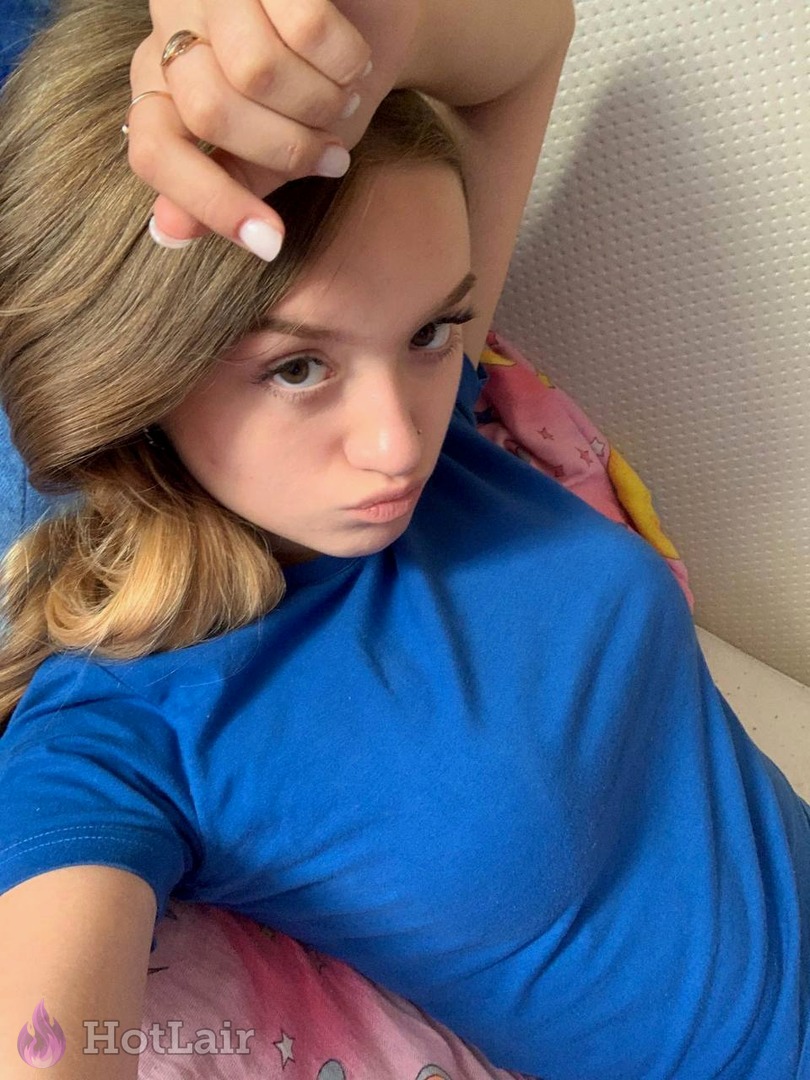 Cute blonde in blue t-shirt lying on bed taking flirty selfie with pouty lips