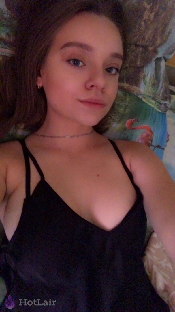 Close-up selfie of attractive young woman in black camisole lying in bed, seductive look with cleavage visible