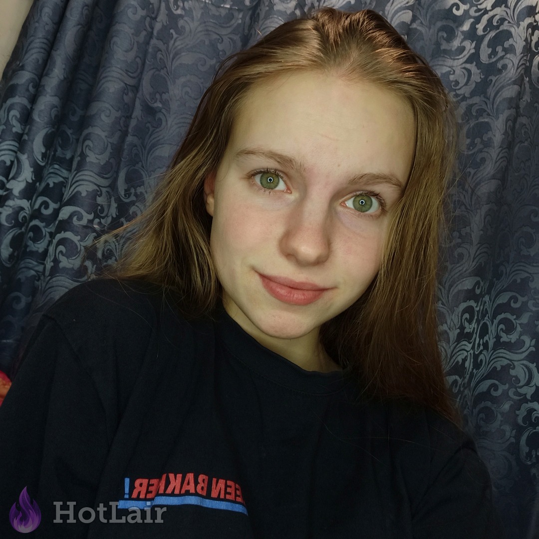 Cute young woman with long light brown hair and striking green eyes smiling sweetly at the camera in a black t-shirt, close-up portrait