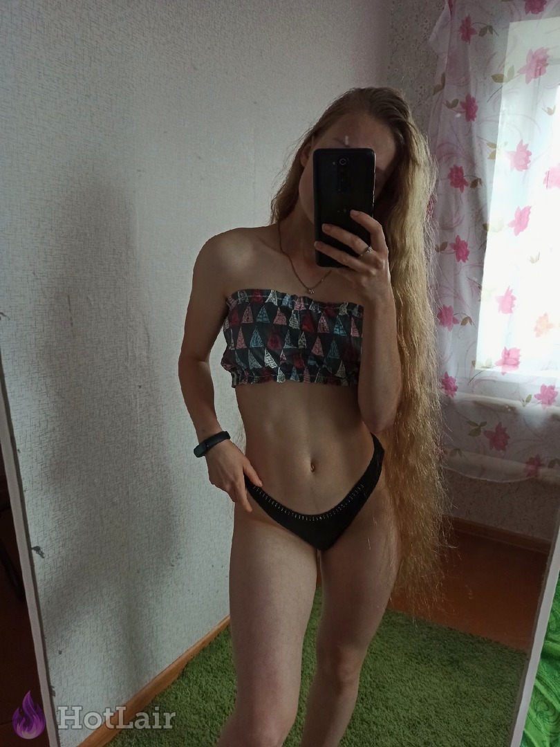 Slender long-haired blonde girl posing in patterned bandeau top and black panties for mirror selfie