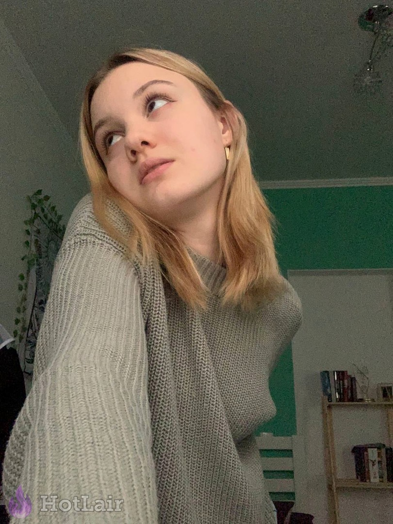 Cute blonde teen in cozy grey knitted sweater looking upwards with innocent expression