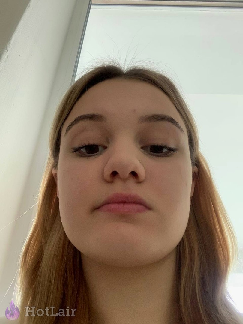 Pretty young woman with long light brown hair and makeup taking close-up selfie by the window