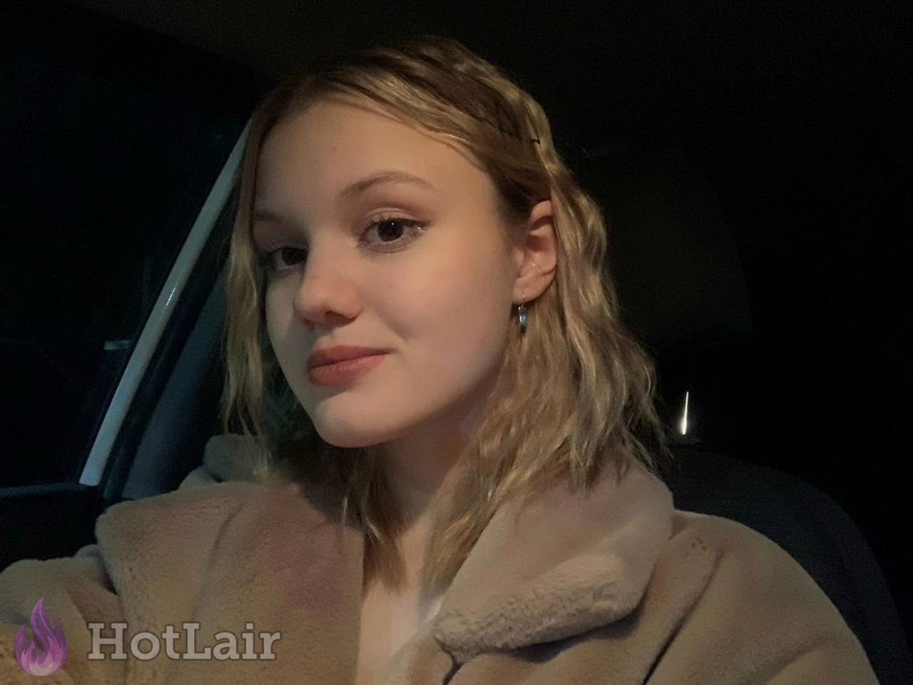 Beautiful blonde teen with makeup taking close-up selfie in car wearing cozy beige fleece jacket