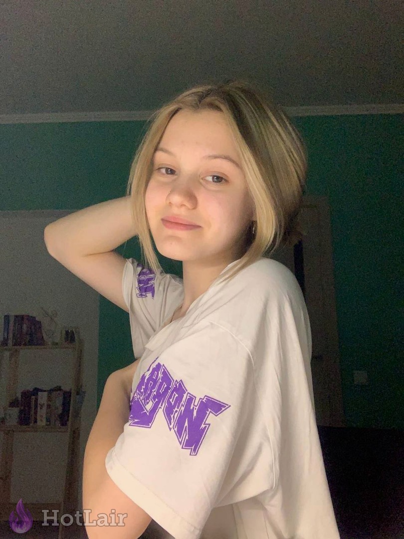 Cute blonde girl in oversized white graphic t-shirt posing with hand behind her head, flirty look