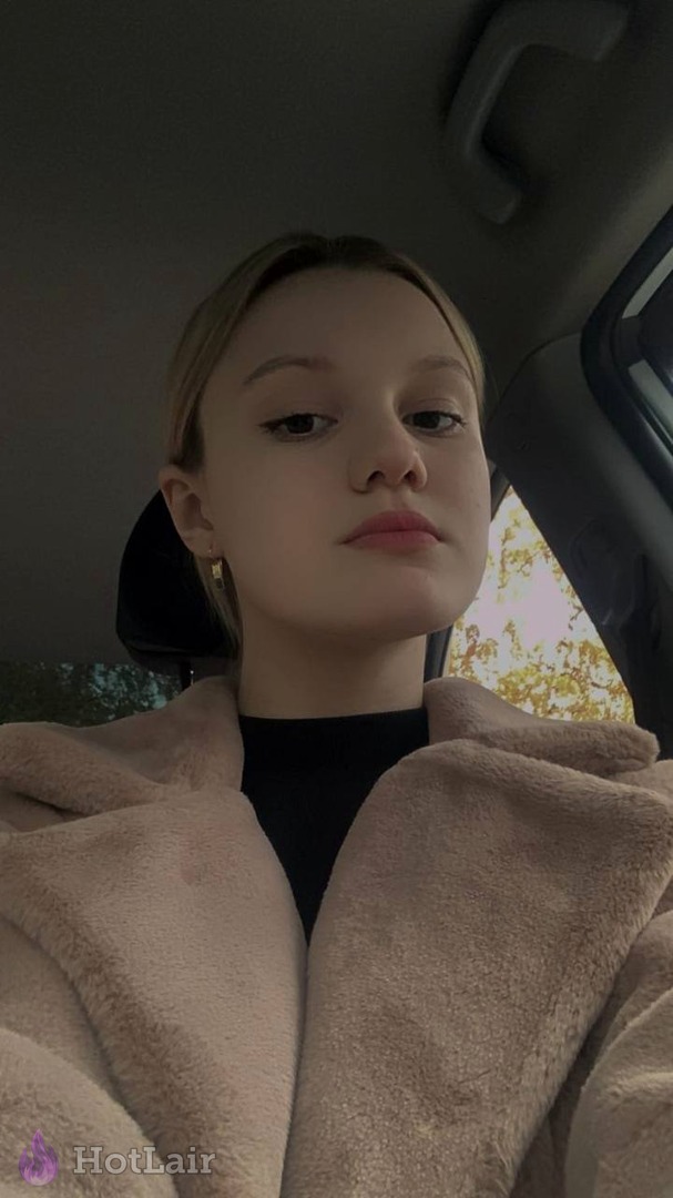 Young blonde girl taking selfie in car wearing soft beige fleece jacket with natural makeup