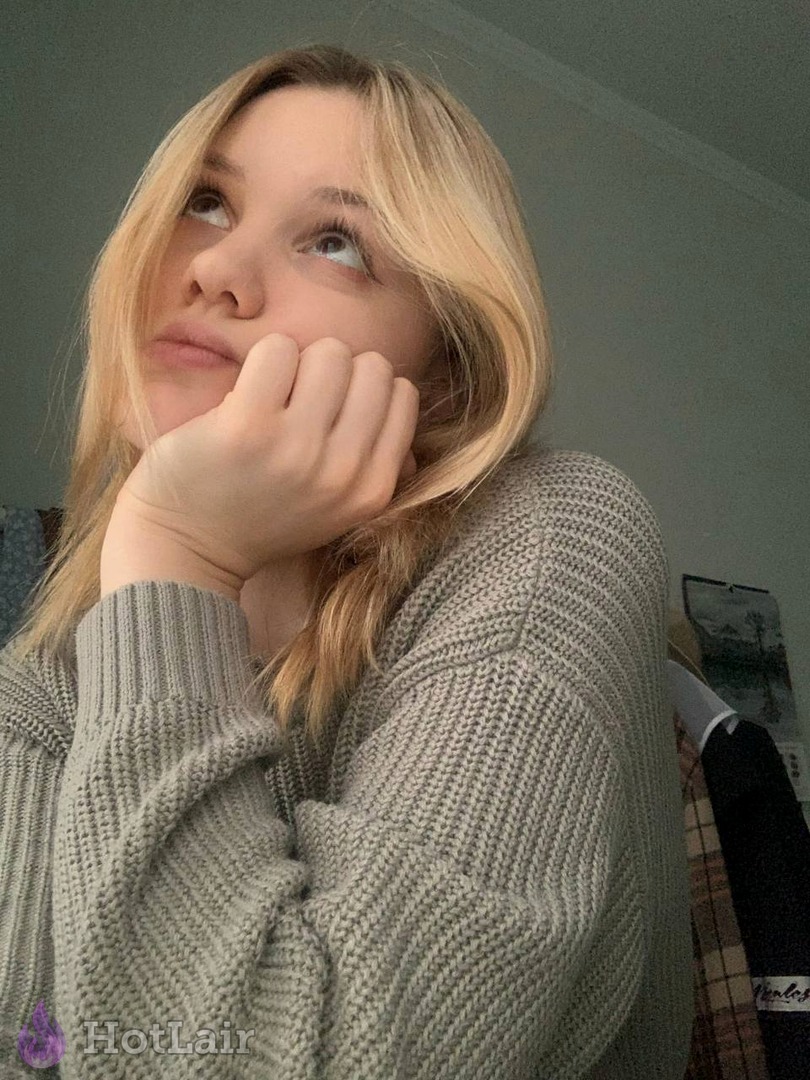Pretty blonde in cozy grey knitted sweater posing with hand on chin looking upwards dreamily