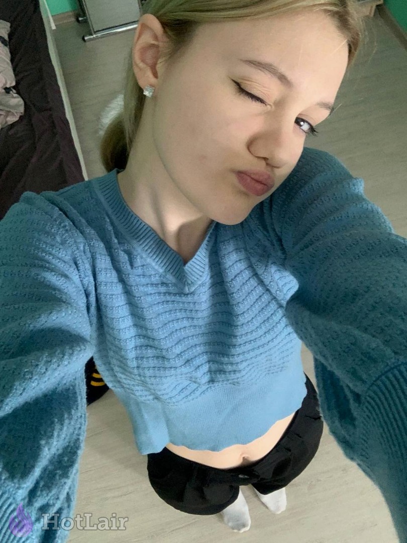 Cute blonde taking selfie in blue cropped knit sweater and black shorts making playful face