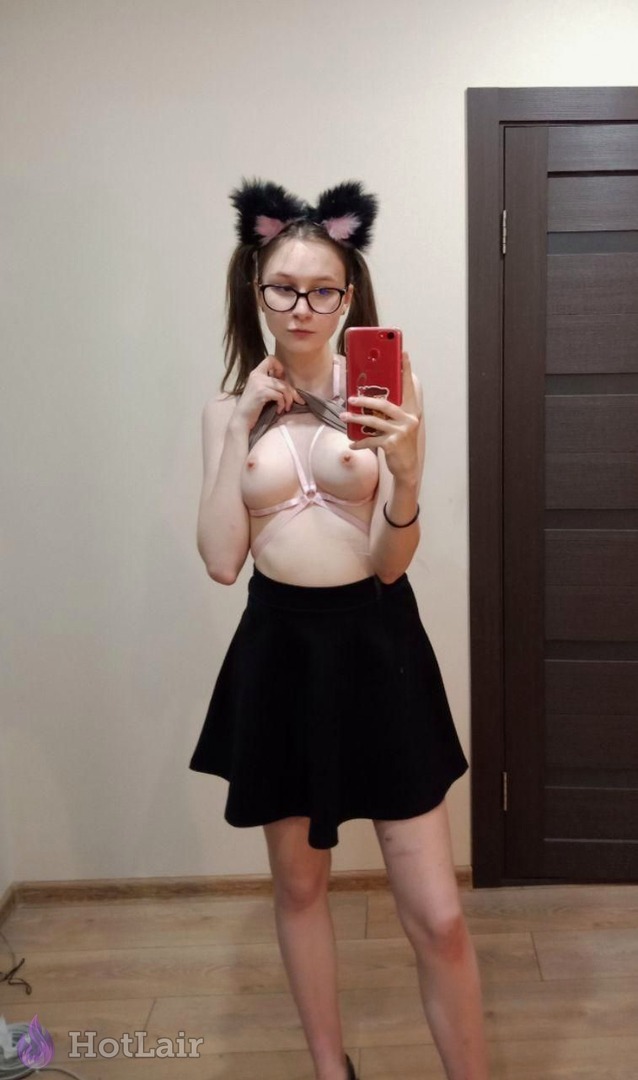 Cute brunette with cat ear headband and glasses taking mirror selfie in pink strappy harness bra