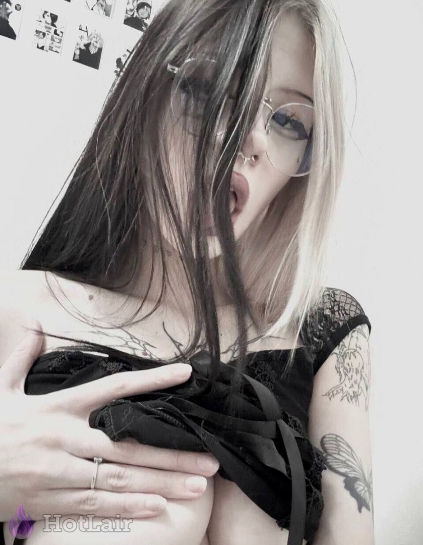 Tattooed blonde with glasses and ahegao expression pulls black top down over her breasts