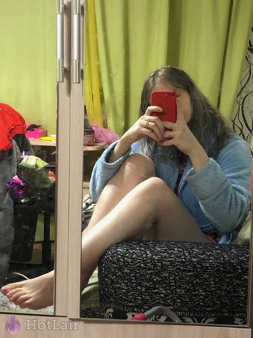 Young brunette taking mirror selfie in blue bathrobe with legs spread holding red phone