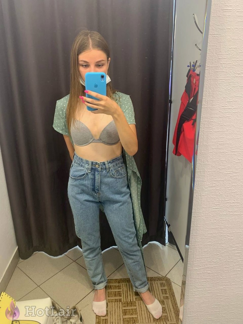 Cute brunette taking mirror selfie in grey push-up bra and blue jeans holding blue phone