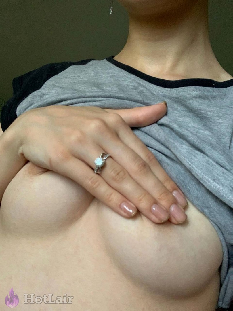 Sensual close-up of large natural breasts with hand wearing ring resting on cleavage under grey shirt