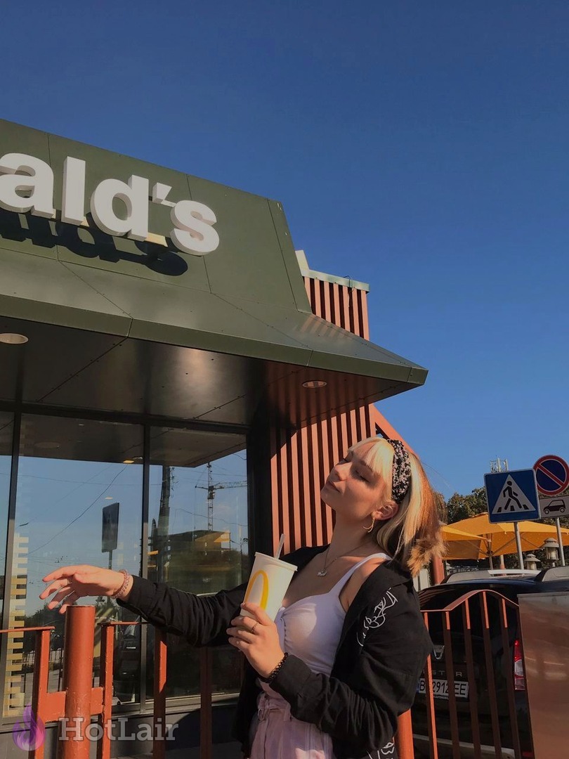 Stylish blonde girl posing casually in front of McDonald’s restaurant on sunny day