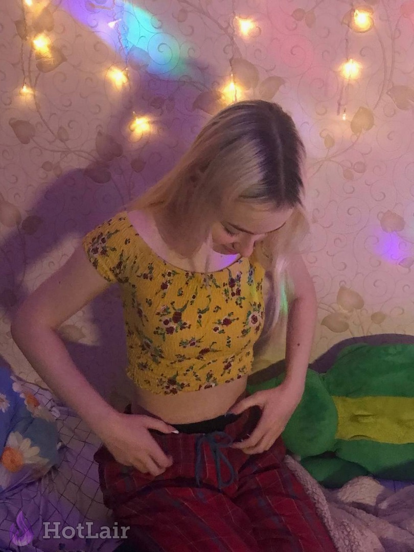 Blonde girl in yellow floral crop top seductively pulling down red plaid pants
