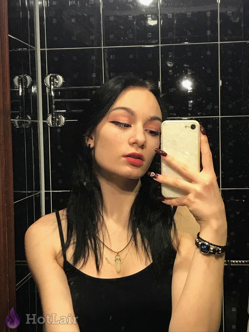 Attractive dark-haired brunette taking mirror selfie in black tank top in bathroom