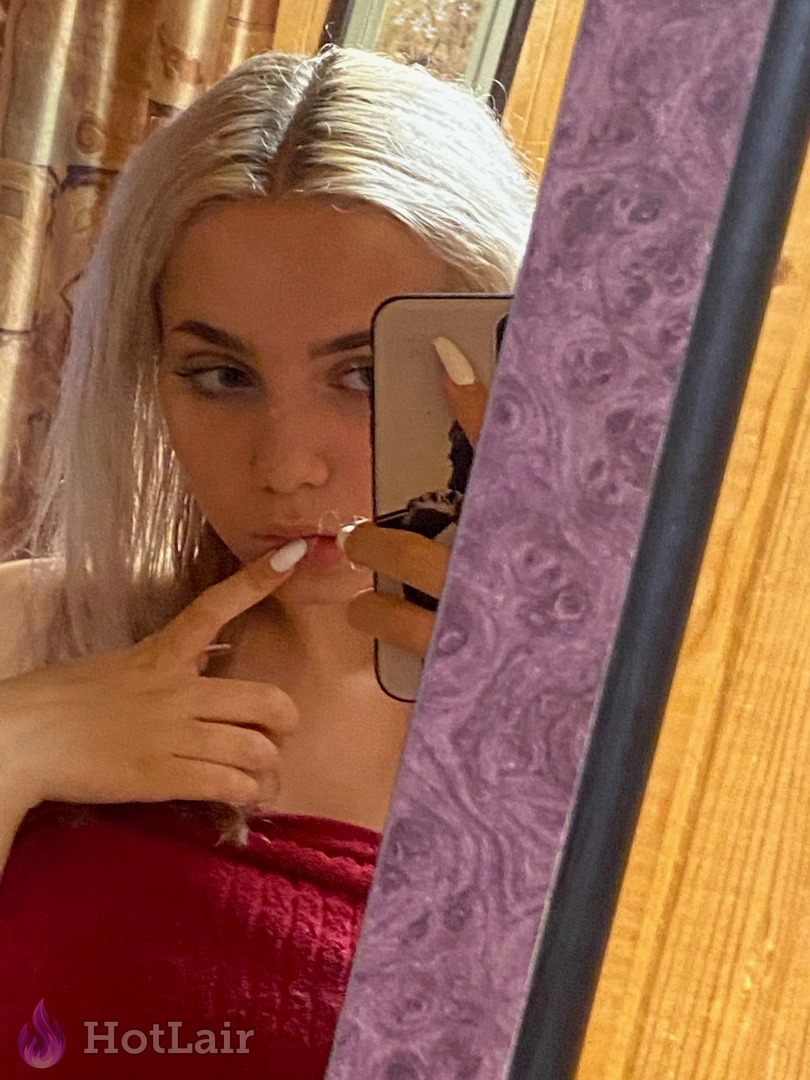Playful platinum blonde taking mirror selfie in red velvet top, finger touching lips seductively with perfect makeup and bedroom eyes