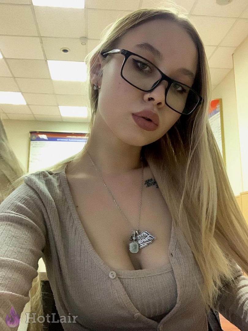 Cute blonde with glasses and long hair taking selfie in low-cut beige cardigan, deep cleavage and flirty expression