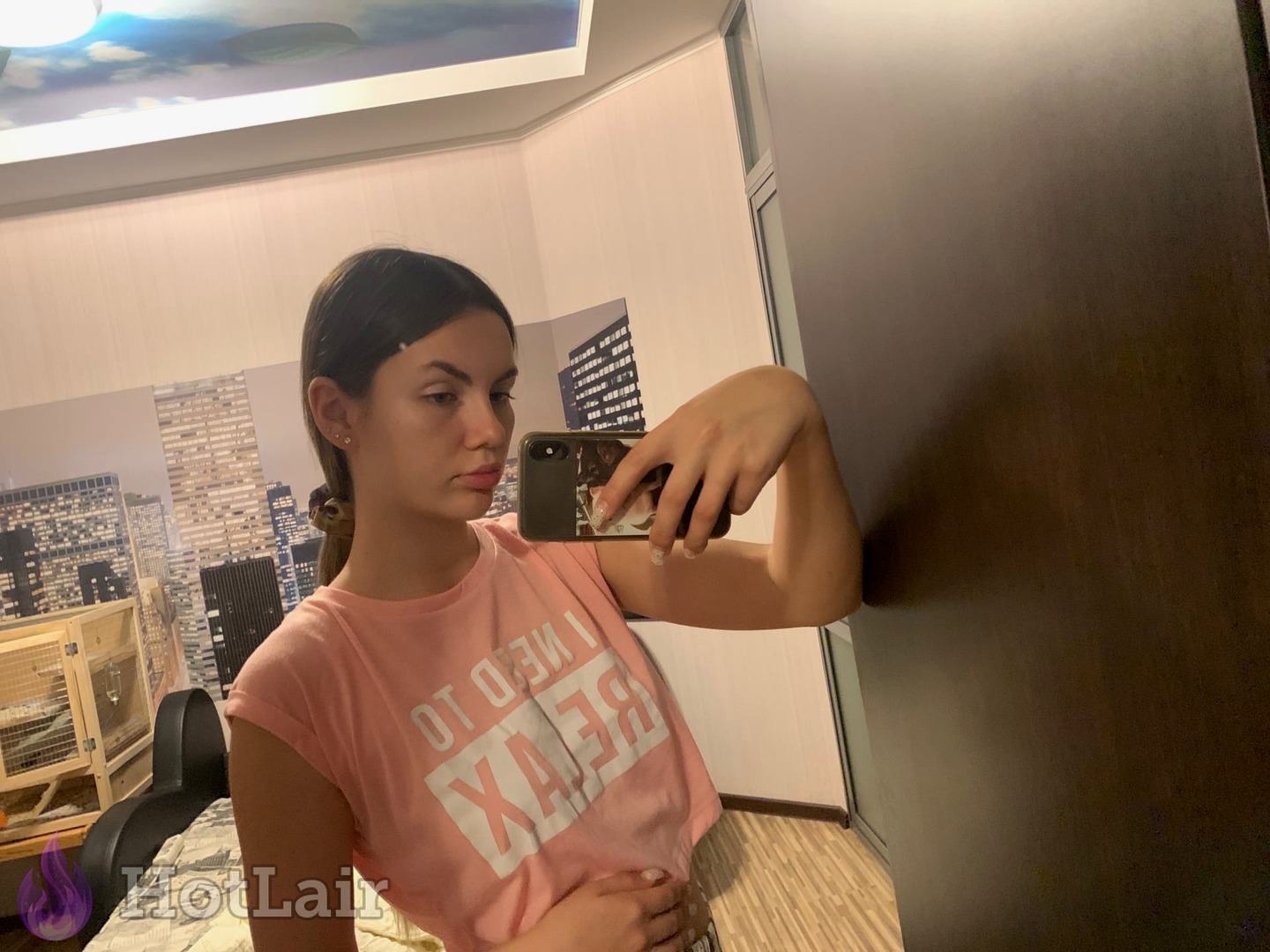 Brunette taking mirror selfie in pink "I NEED TO RELAX" t-shirt with flirty expression and bedroom eyes