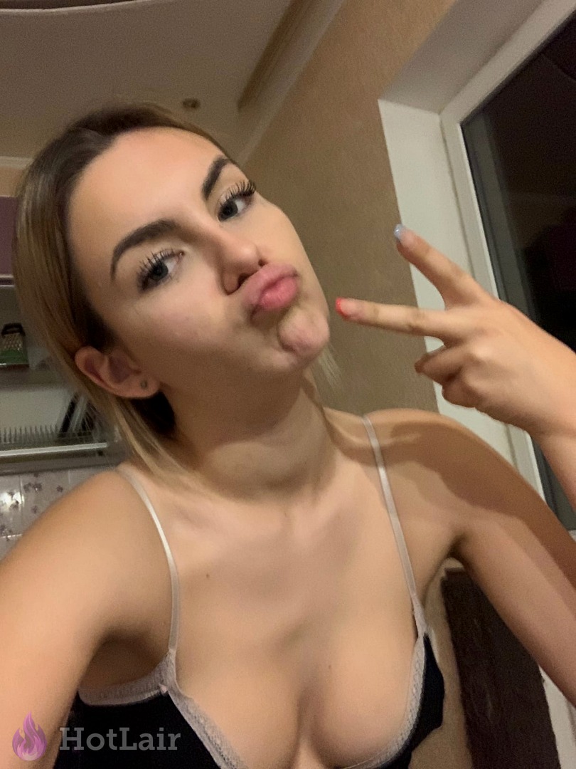 Playful blonde making duck face and peace sign in black lace bra, flirty selfie