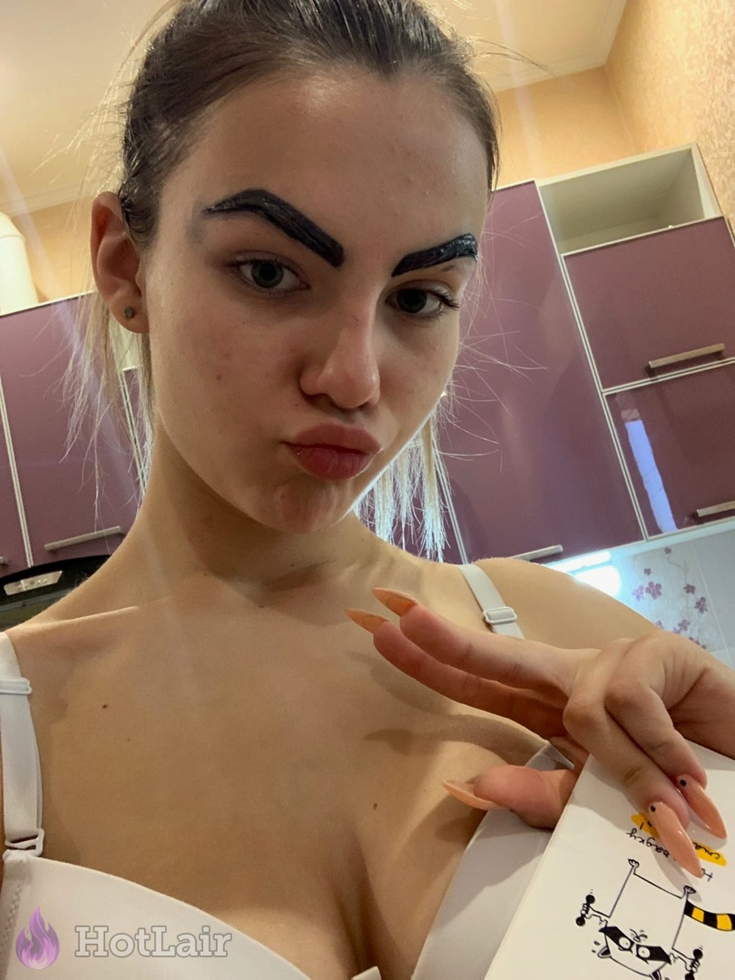 Girl with dramatic black eyebrows making duck face in white bra, long nails selfie
