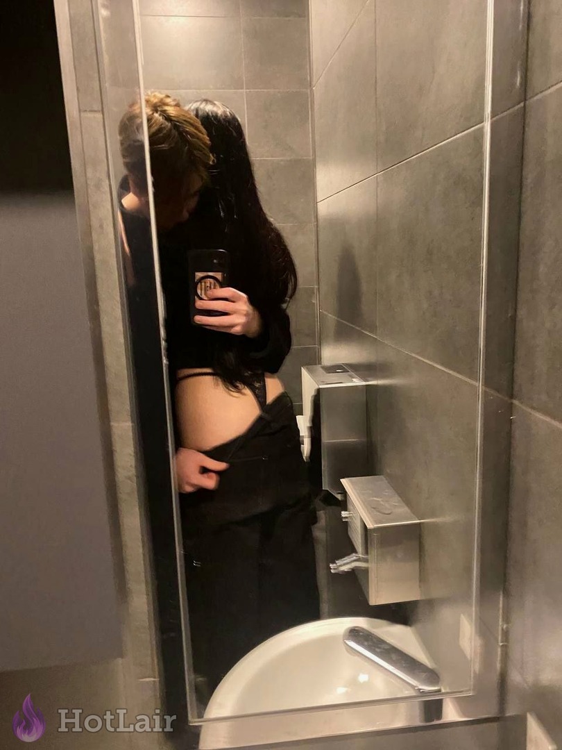 Brunette taking mirror selfie in bathroom pulling down black pants to teasingly show her ass in thong