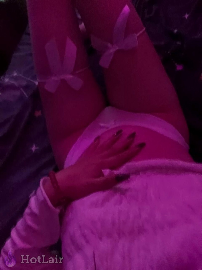 Woman in pink lingerie and bow stockings lying seductively on bed touching her body under magenta light