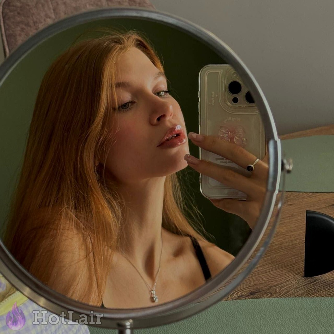 Beautiful redhead taking close-up mirror selfie with glossy lips and delicate jewelry