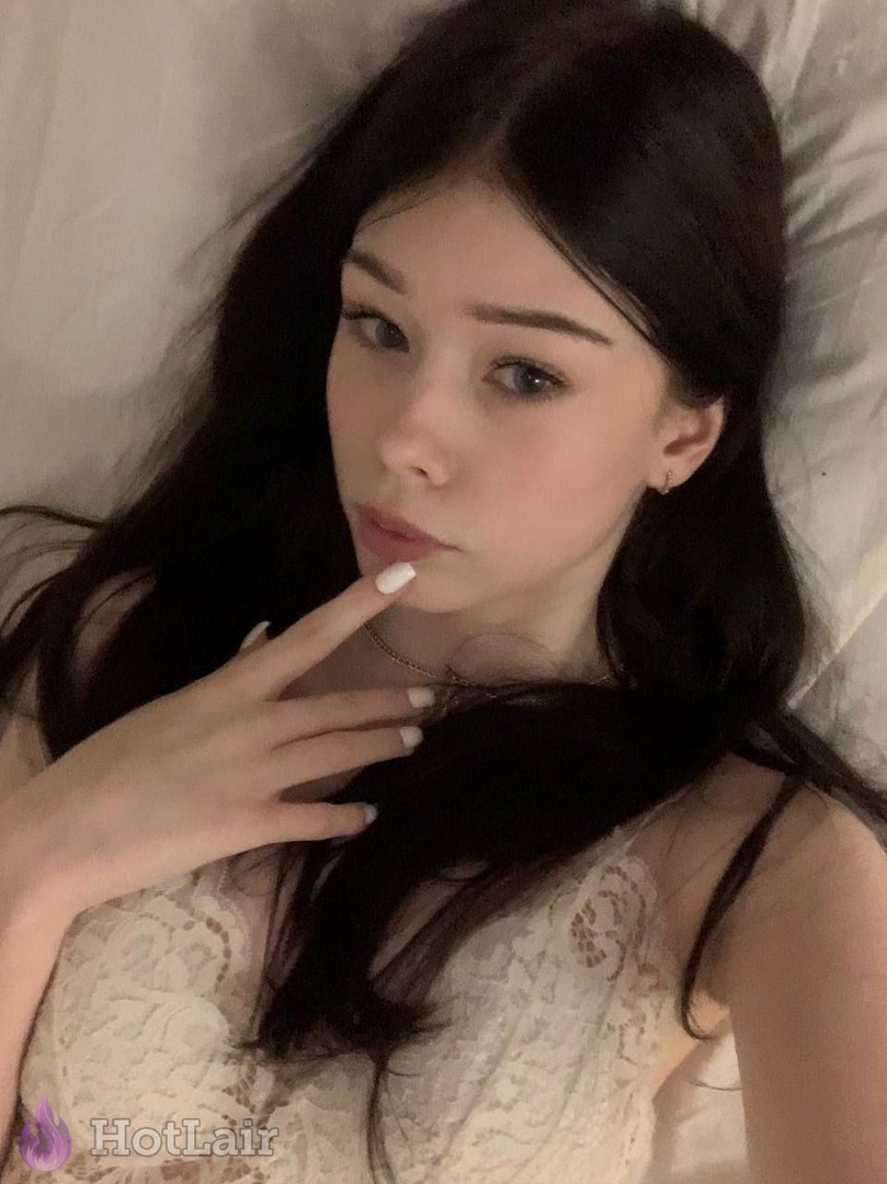 Stunning long-haired brunette in white lace top lying on bed looking at camera with hand near face