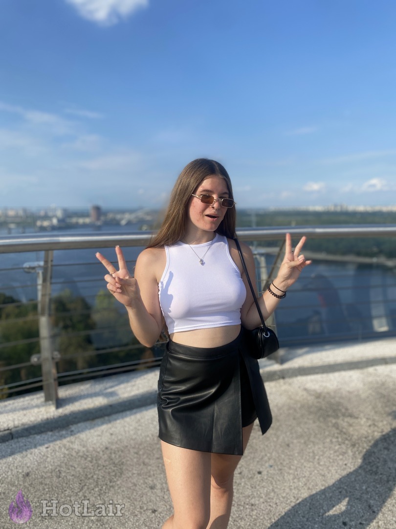 Attractive young woman in white crop top and black mini skirt posing on a sunny rooftop terrace