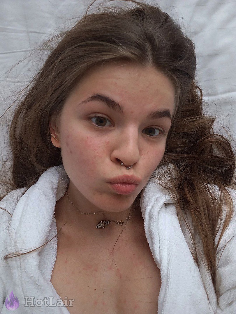 Cute brunette with nose ring and acne making duck face selfie while wearing white bathrobe