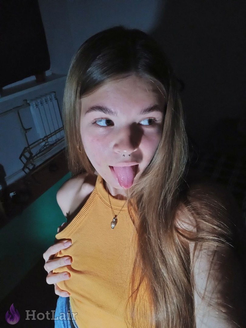 Playful young woman with nose piercing sticking her tongue out in yellow tank top for close-up selfie